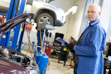Mechanic with notebook during car conditioner refilling