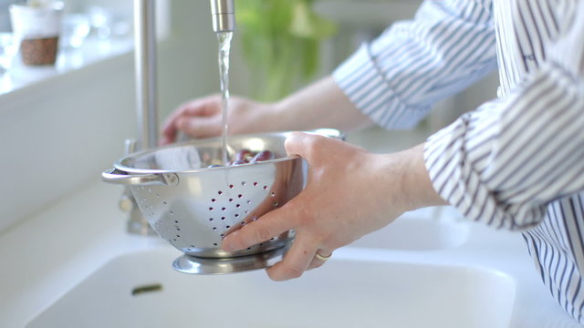 Man walks into shot and washes red grapes in steel colander