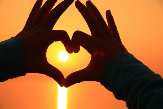 hands make heartshape against sunset seaside