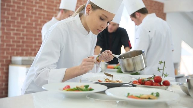 Young woman in cooking class pouring sauce on plate