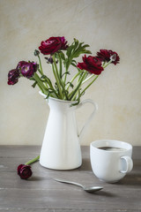 Vase mit Ranunkeln und Tasse Kaffee