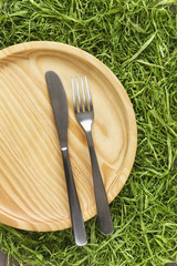 Holzteller mit Besteck auf Gras, Picknick, Frühling