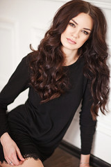 Young brunette lady in black lacy dress posing in white room. 