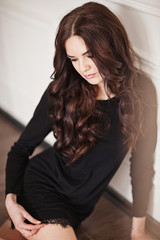Fototapeta premium Young brunette lady in black lacy dress posing in white room. 