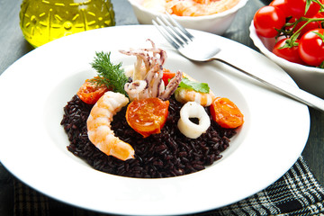 Black rice with sliced squids ,prawns and tomato on white plate