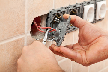 Electrician hands installing wires into a wall fixture