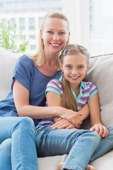 Smiling mother and daughter sitting together on sofa at home