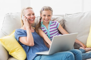 Happy mother and daughter using technologies on sofa
