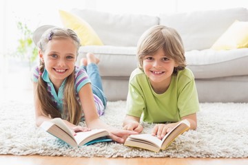 Happy siblings holding books while lying on rug