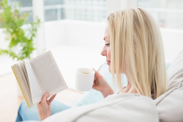 Woman reading book while having coffee on sofa
