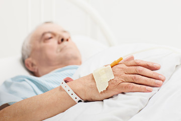 Senior lying in a hospital bed with iv set on his hand