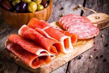slices of prosciutto  with salami and olives on a cutting board