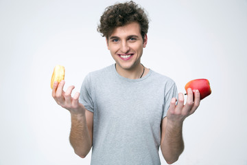 Smiling man holding apple and donut over gray background