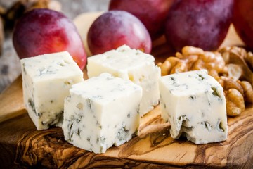 Blue cheese close-up with grape and nuts on a wooden board