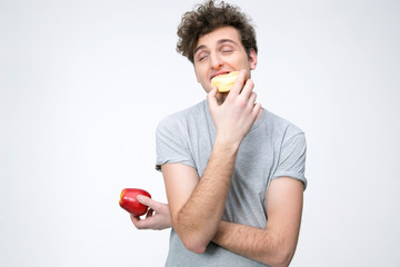 Young man holding apple and eating unhealthy donut