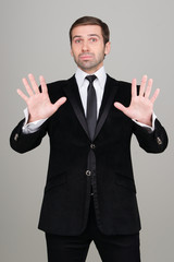 Young business man in black suit making calm down gesture. Studi
