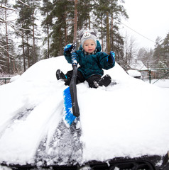 Funny baby boy cleans car bonnet from snow