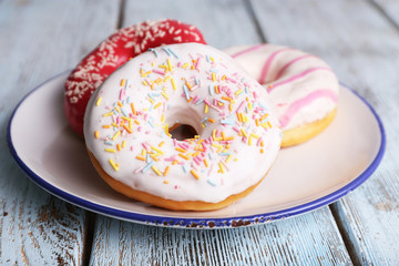 Delicious donuts with icing on plate on wooden background