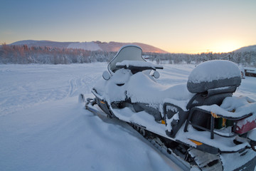 Snowmobile parked in Levi, Finland; back view of a machine covered by fresh snow during sunset