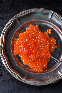 Salmon caviar on metal plate over dark background