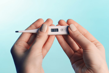 Female hands holding thermometer on blue background