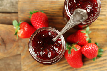 Jars of strawberry jam with berries on wooden background