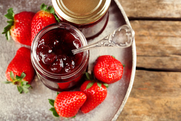 Jars of strawberry jam with berries on tray on table close up