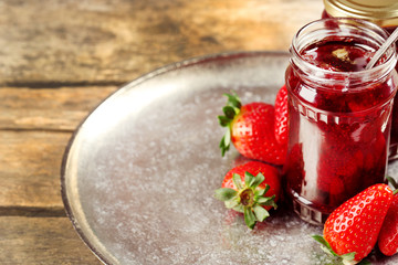Jars of strawberry jam with berries on wooden background