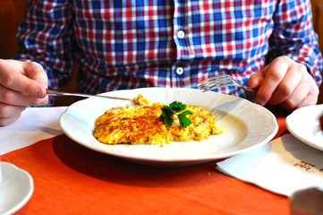 Rührei, ein Omelet liegt auf dem Teller. Ein Mann wird es mit Messer und Gabel verspeisen.