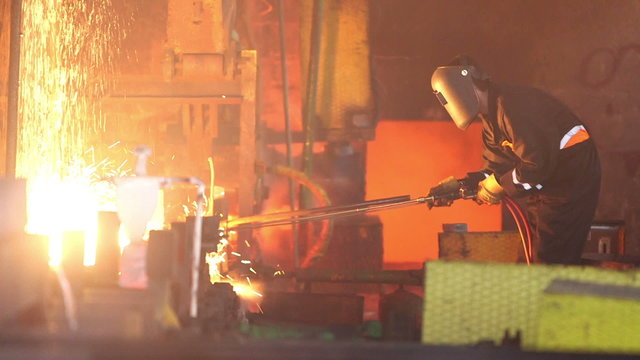 Steel making - male worker cuts fiery steel blocks at the factory