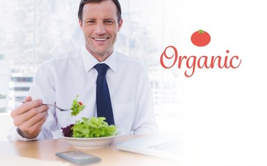 Organic against happy businessman eating a salad on his desk