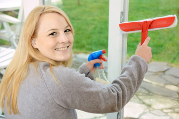 Frau putzt Fensterscheibe mit Glasreiniger