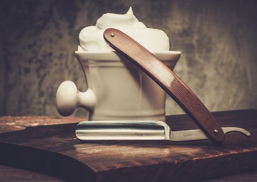 Shaving bowl and straight razor on wooden background