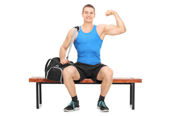 Obraz premium Muscular athlete showing his bicep seated on a bench