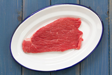 raw meat on white dish on blue background