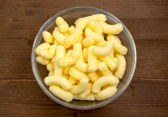 Corn snacks on bowl on wooden table seen from above