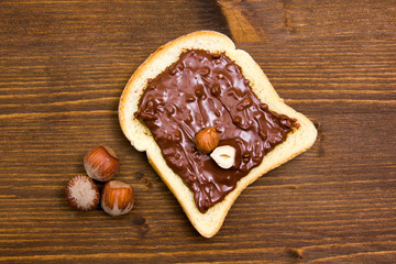 Slice of bread with chocolate with hazelnuts on wood from above
