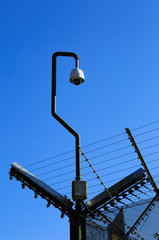 Security camera on the corner of a fence with wires.