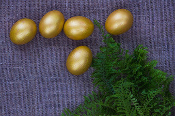 Golden eggs and fern leaves on a linen background.