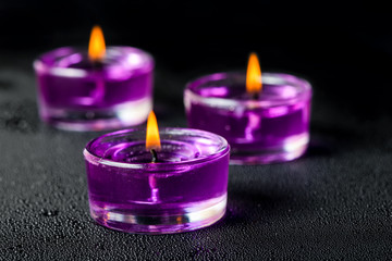 Obraz na płótnie Canvas purple candles on a black background with water drops, closeup