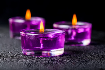 Obraz na płótnie Canvas three beautiful purple candles on a black background with water