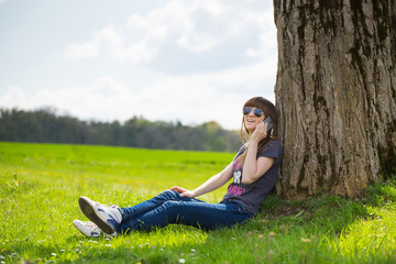 Smiling brunette woman leaning on tree and talking on mobile pho