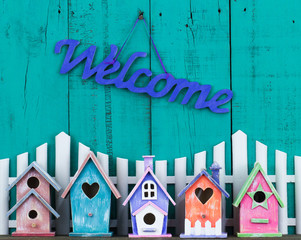 Welcome sign by white picket fence and colorful birdhouses