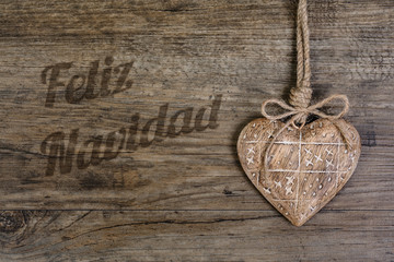 Wooden heart on vintage oak background and caption "Feliz Navida