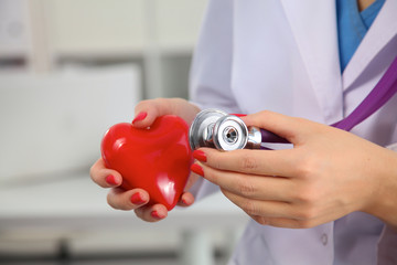 Doctor with stethoscope examining red heart, isolated on white