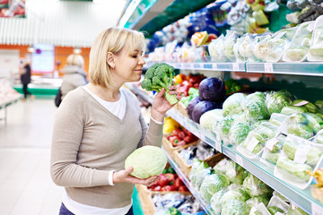 Woman sniffs broccoli and holds white cabbage in store
