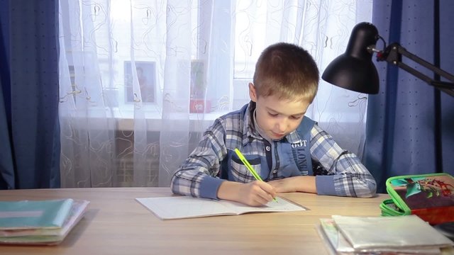 child doing homework, writing in a notebook in the evening at