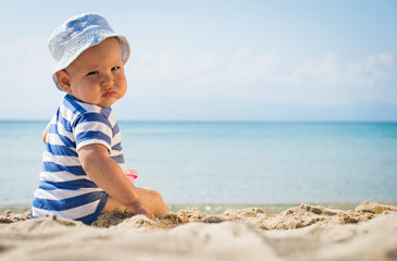Baby boy hat sitting beach.