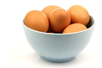 blue bowl with fresh brown eggs on a white background