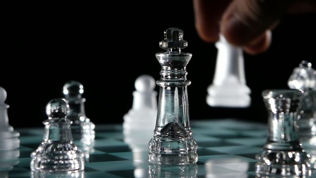 Close up, glass chess pieces over black background. Slow motion